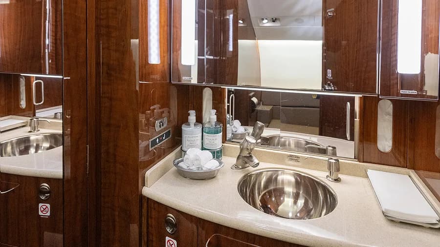 A luxurious aircraft lavatory with two sinks, polished wood cabinetry, and large mirrors.