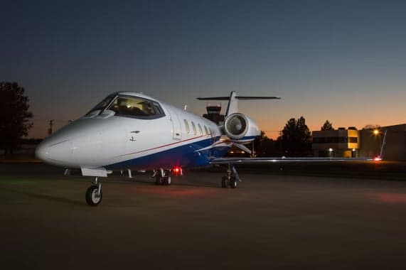 Learjet on the tarmac at dusk with blue and white paint scheme.