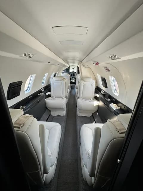 The interior cabin of a business jet, showing rows of light-colored leather seats and an aisle.