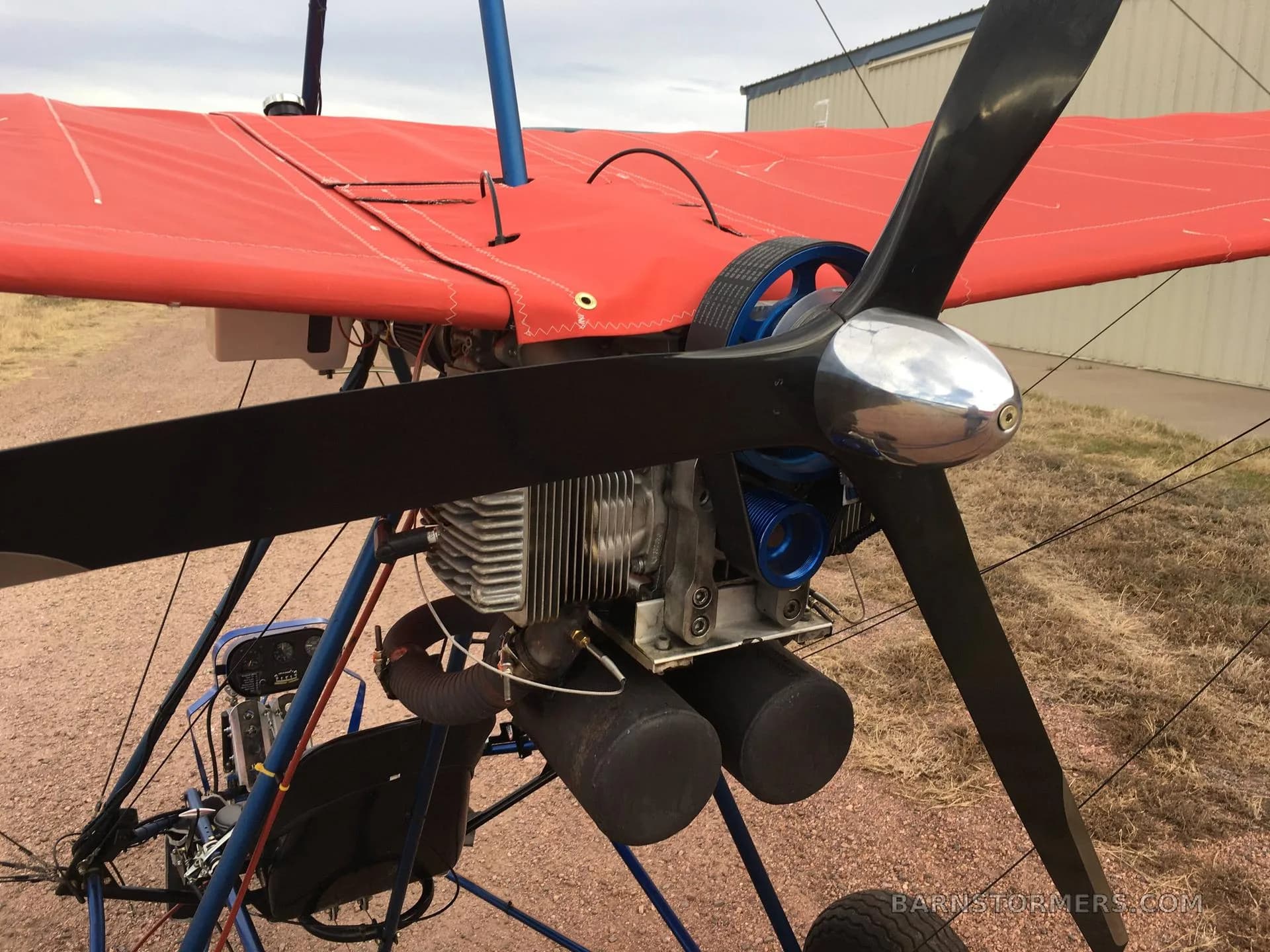 A close-up view of the engine and propeller of a red ultralight aircraft.