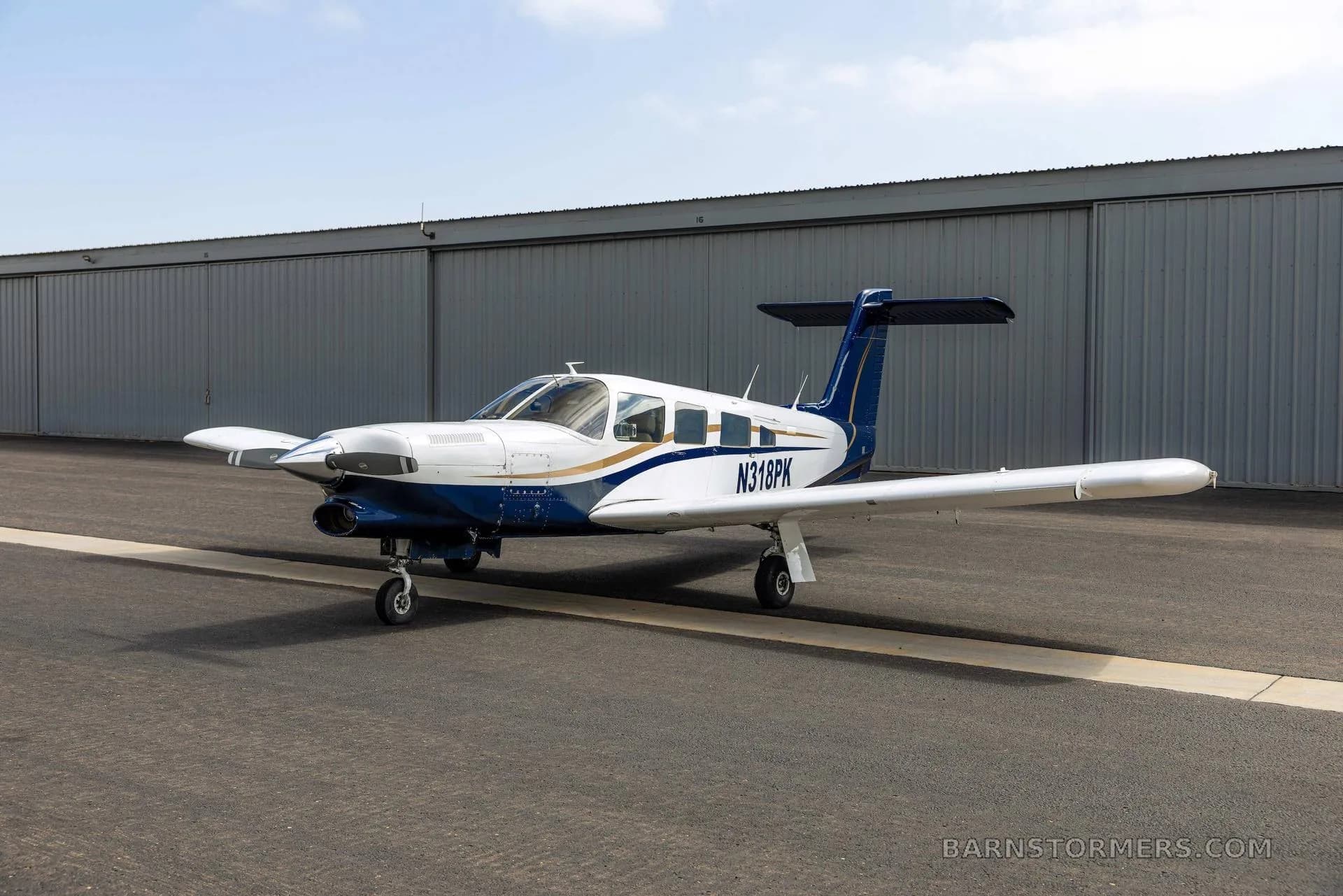 A three-quarter front view of a white and blue single-engine propeller aircraft with tail number N318PK, parked on an asphalt tarmac.