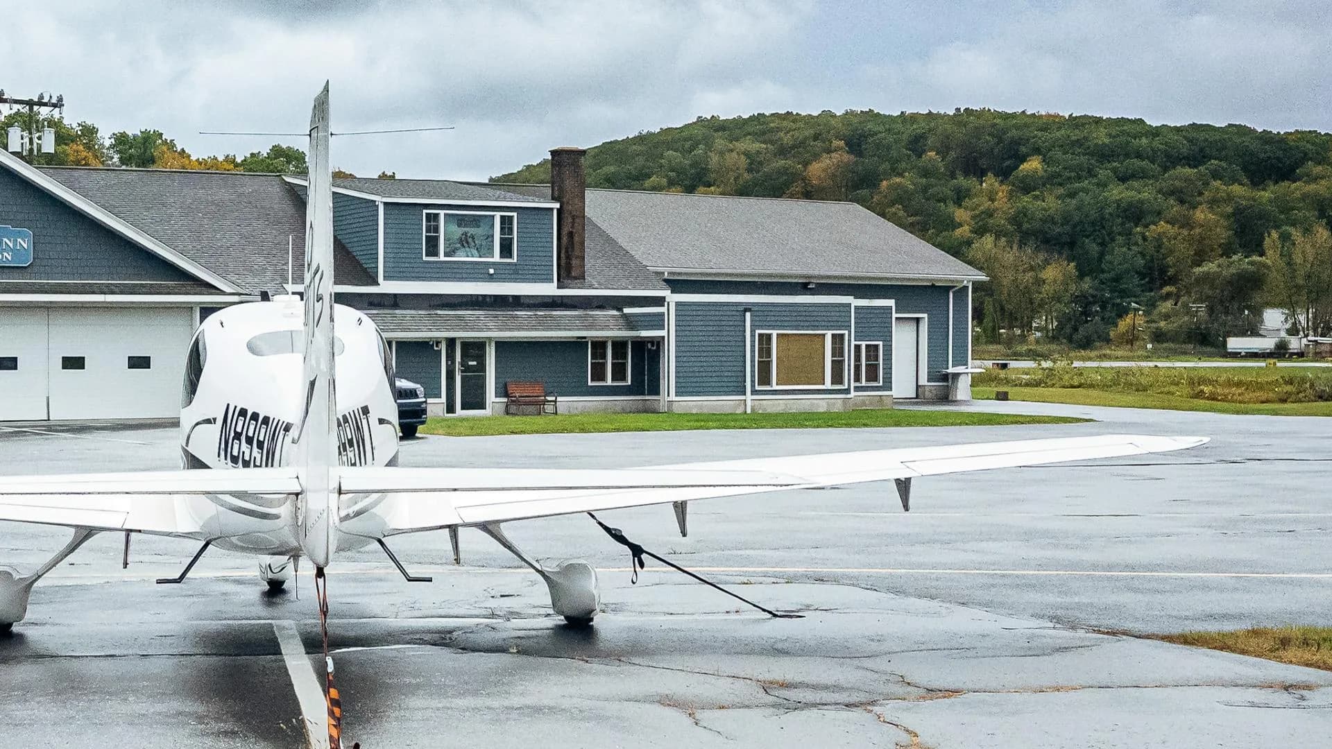 A rear view of a white Cirrus SR20 aircraft with registration N899WT, parked on a wet tarmac in front of a blue building.
