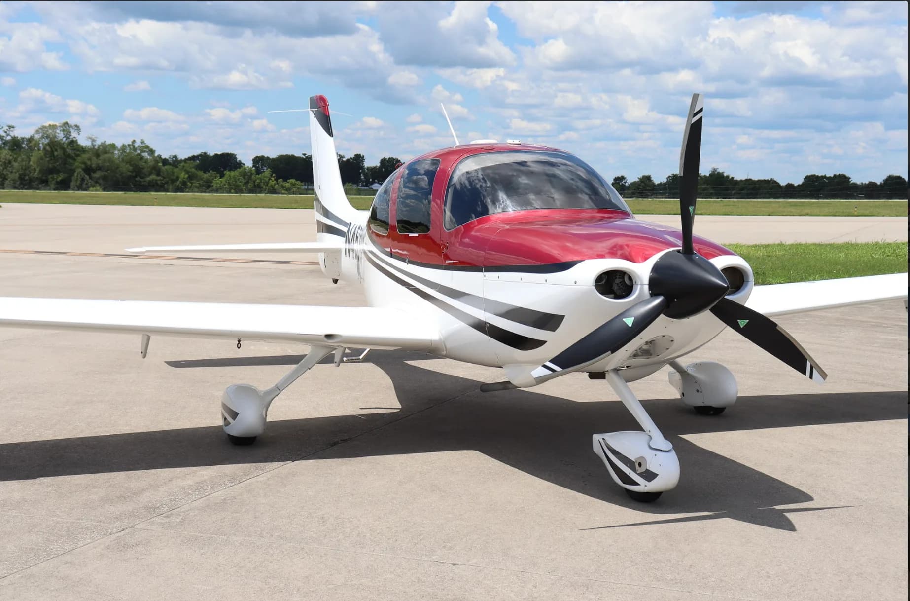 A three-quarter front view of a white and red single-engine aircraft with its doors closed on an airfield.