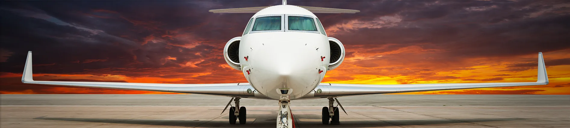 Front view of a private jet against a dramatic sunset.