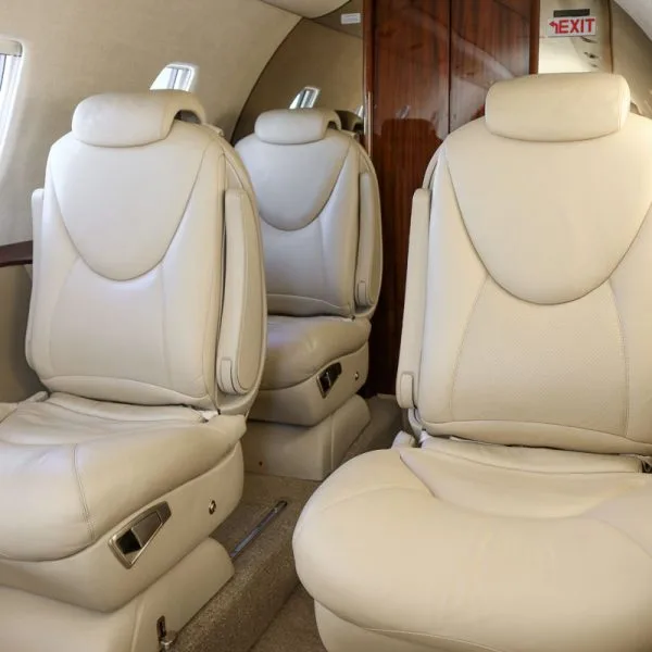 Close-up of light beige leather seats in a private jet cabin, facing a dark wood partition.