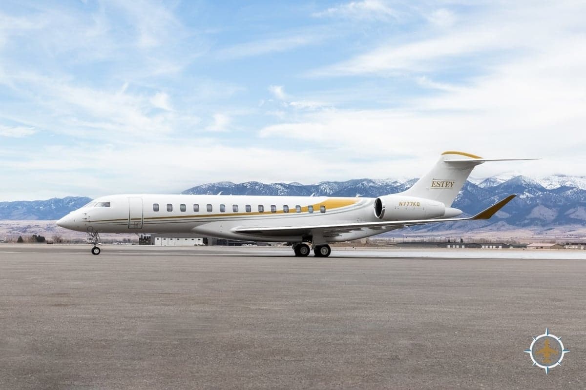 A Bombardier Global Express, registration N777KQ, sits on the tarmac with mountains in the background.