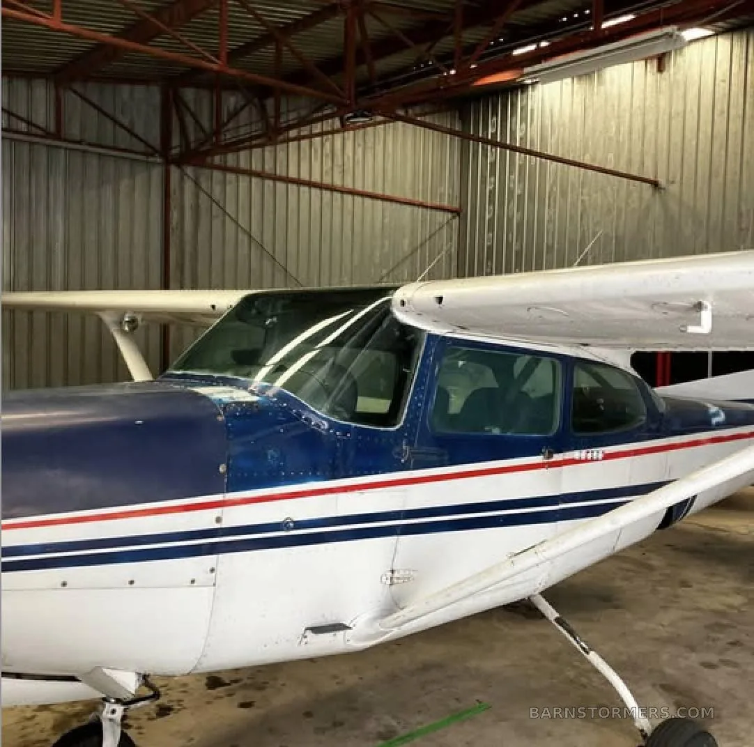 A close-up side view of the cockpit and front fuselage of a blue and white aircraft inside a hangar.