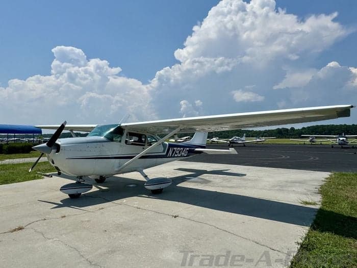 A Cessna 172 Skyhawk with a white and blue paint scheme is parked on the tarmac.