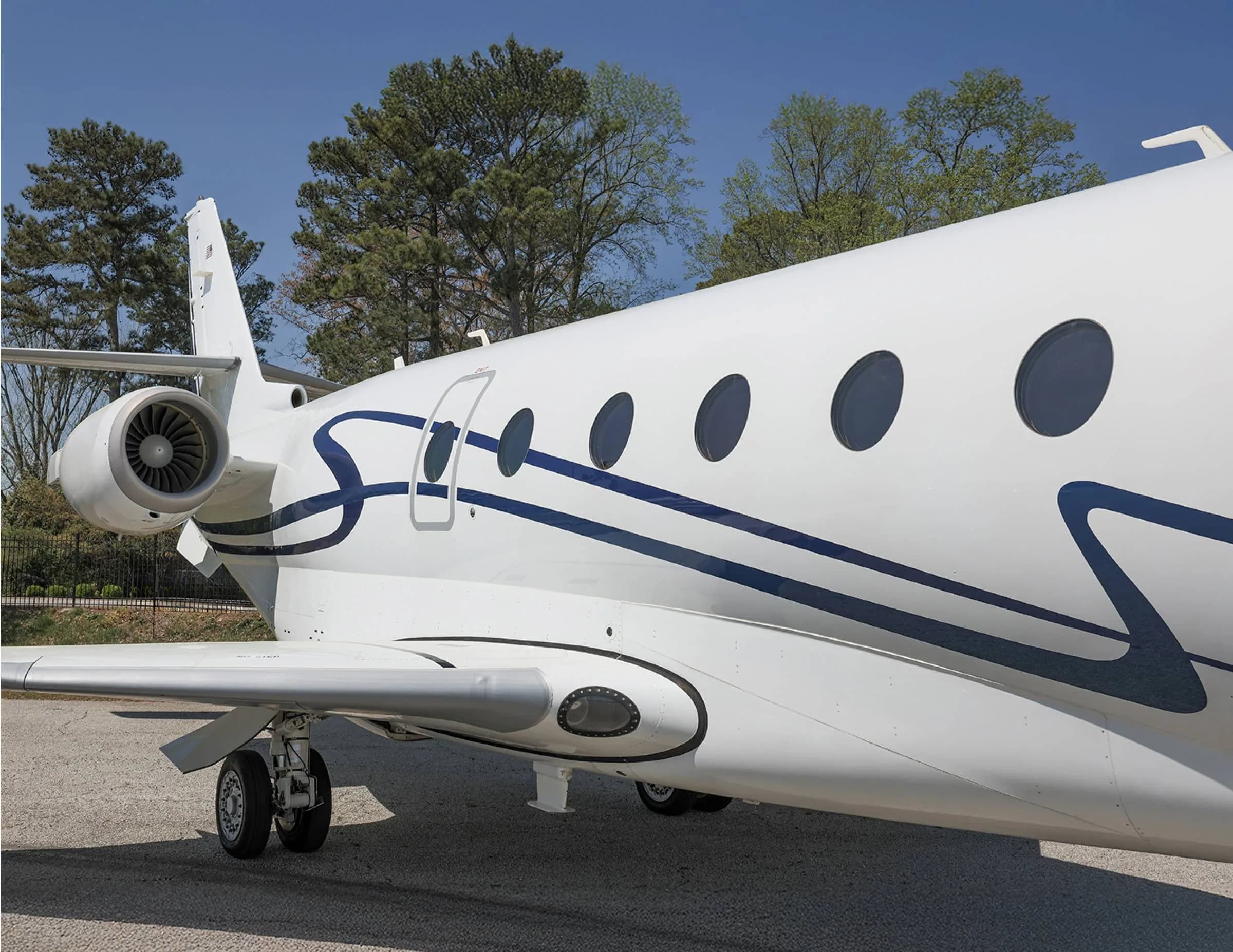 Side view of a white aircraft with blue accents parked on the tarmac, showing the engine and windows.