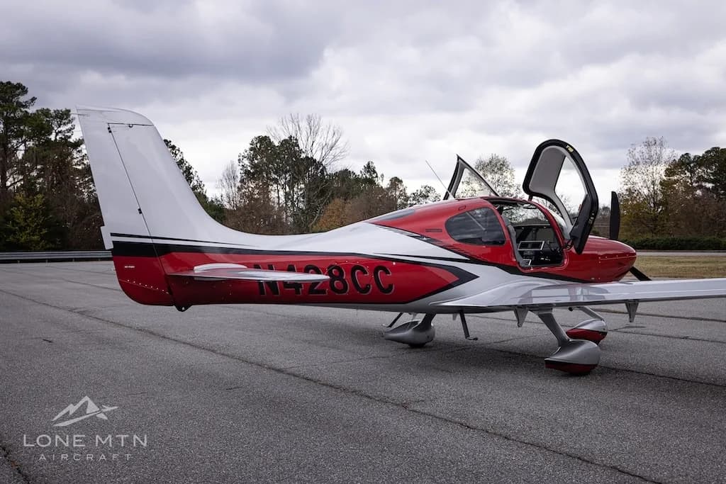 A side view of the red and silver Cirrus Vision Jet (N428CC) with its doors open, parked on an asphalt tarmac.