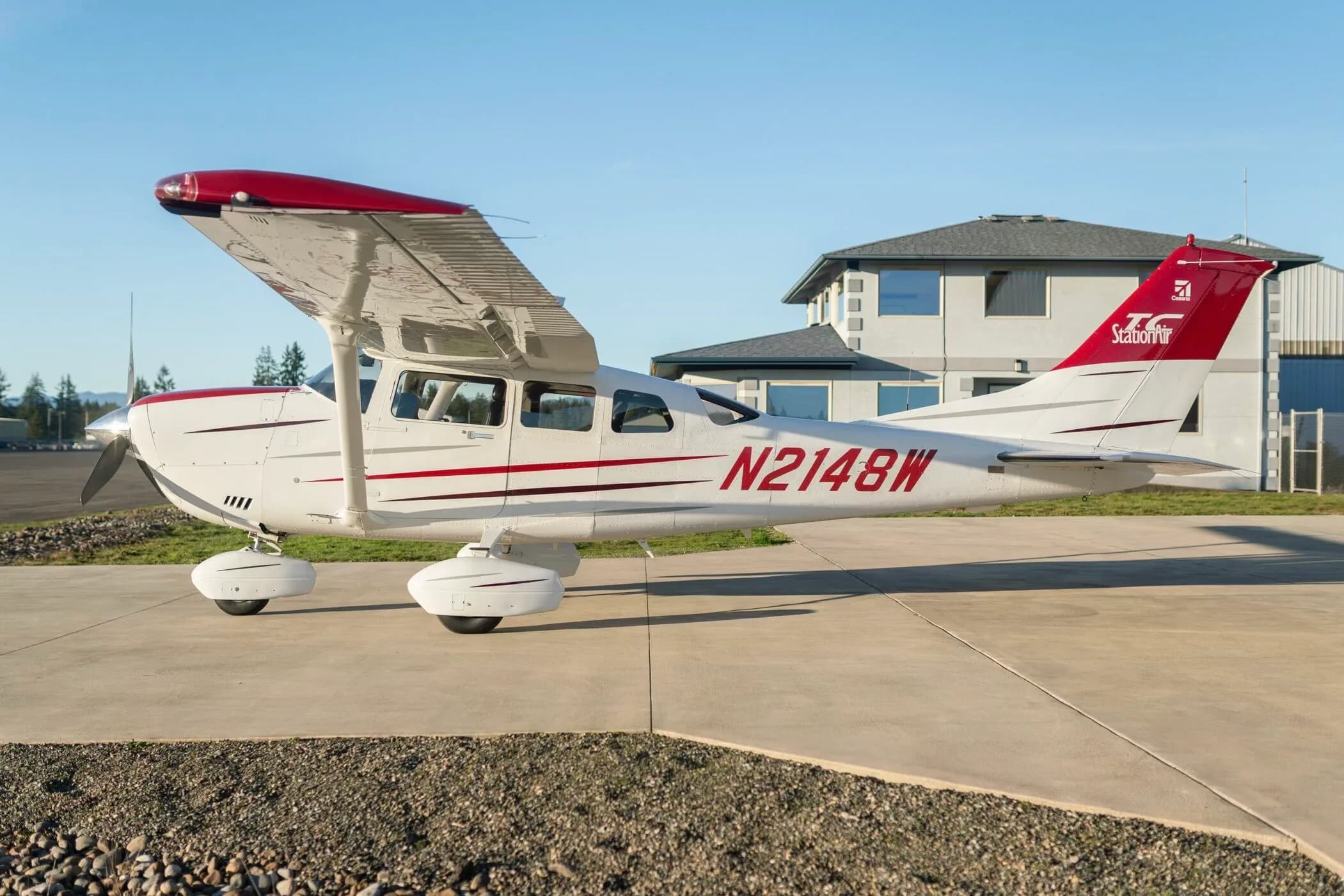 A white Cessna aircraft with red and dark red stripes, registration N2148W, parked on a tarmac with a building in the background.