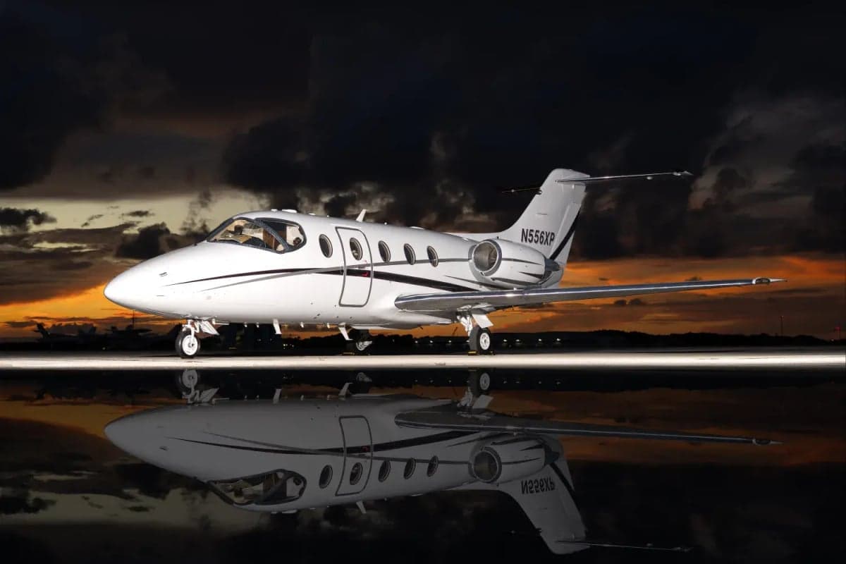A white Learjet is reflected on the tarmac at sunset.