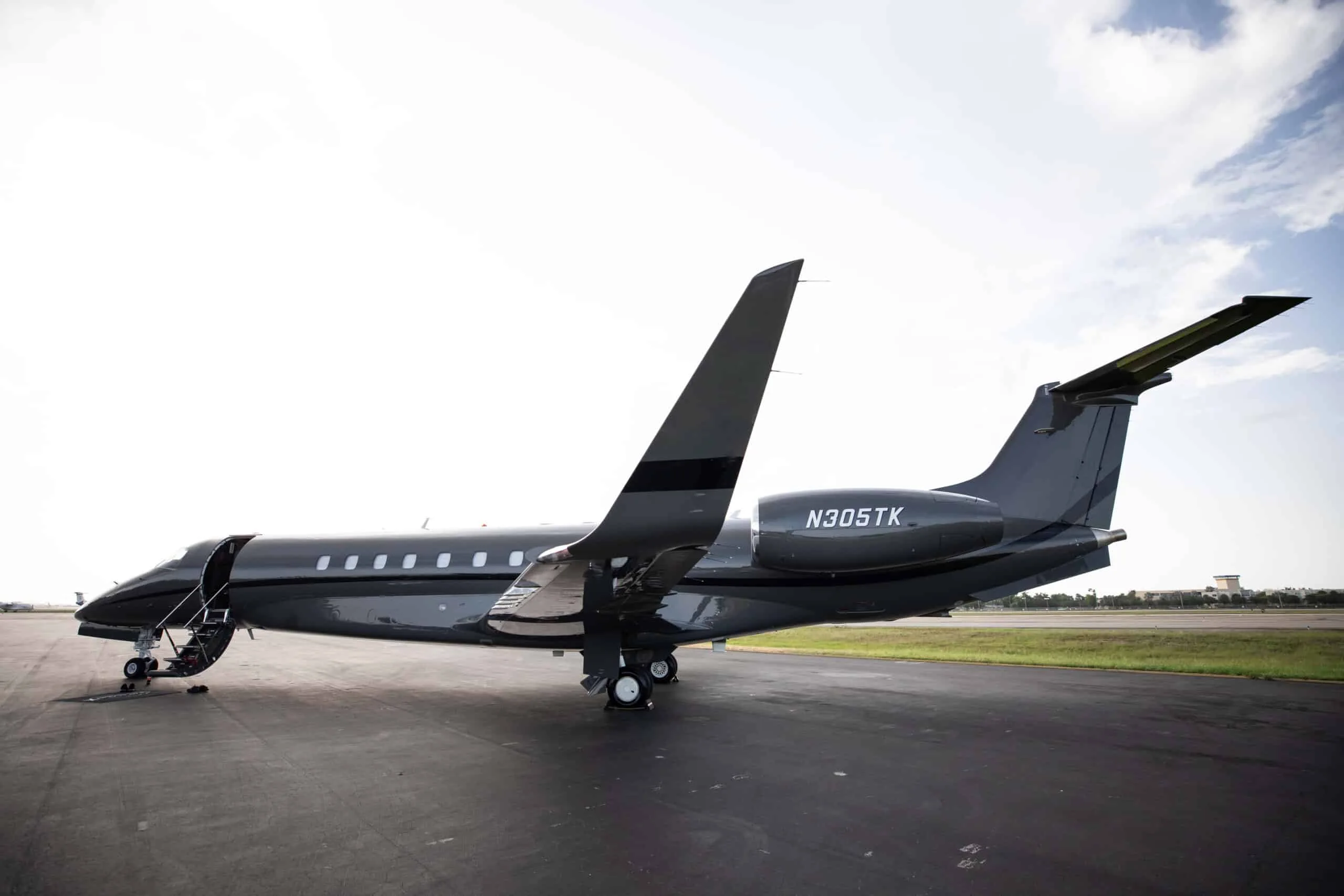 A rear view of the dark grey Embraer Legacy 500 business jet, registration N305TK, parked on a tarmac with its main door open.