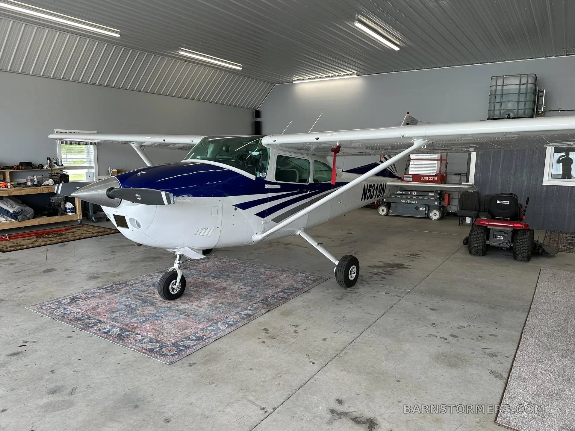 A white and blue Cessna aircraft with registration N5319N is parked inside a hangar on a decorative rug.