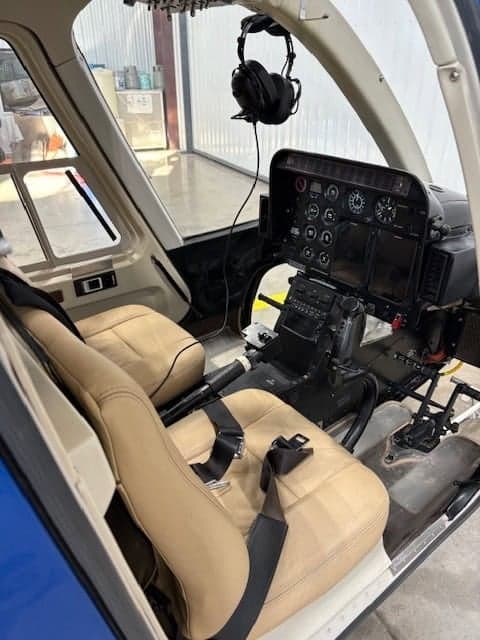 The cockpit of the helicopter is shown with tan seats and a black instrument panel.