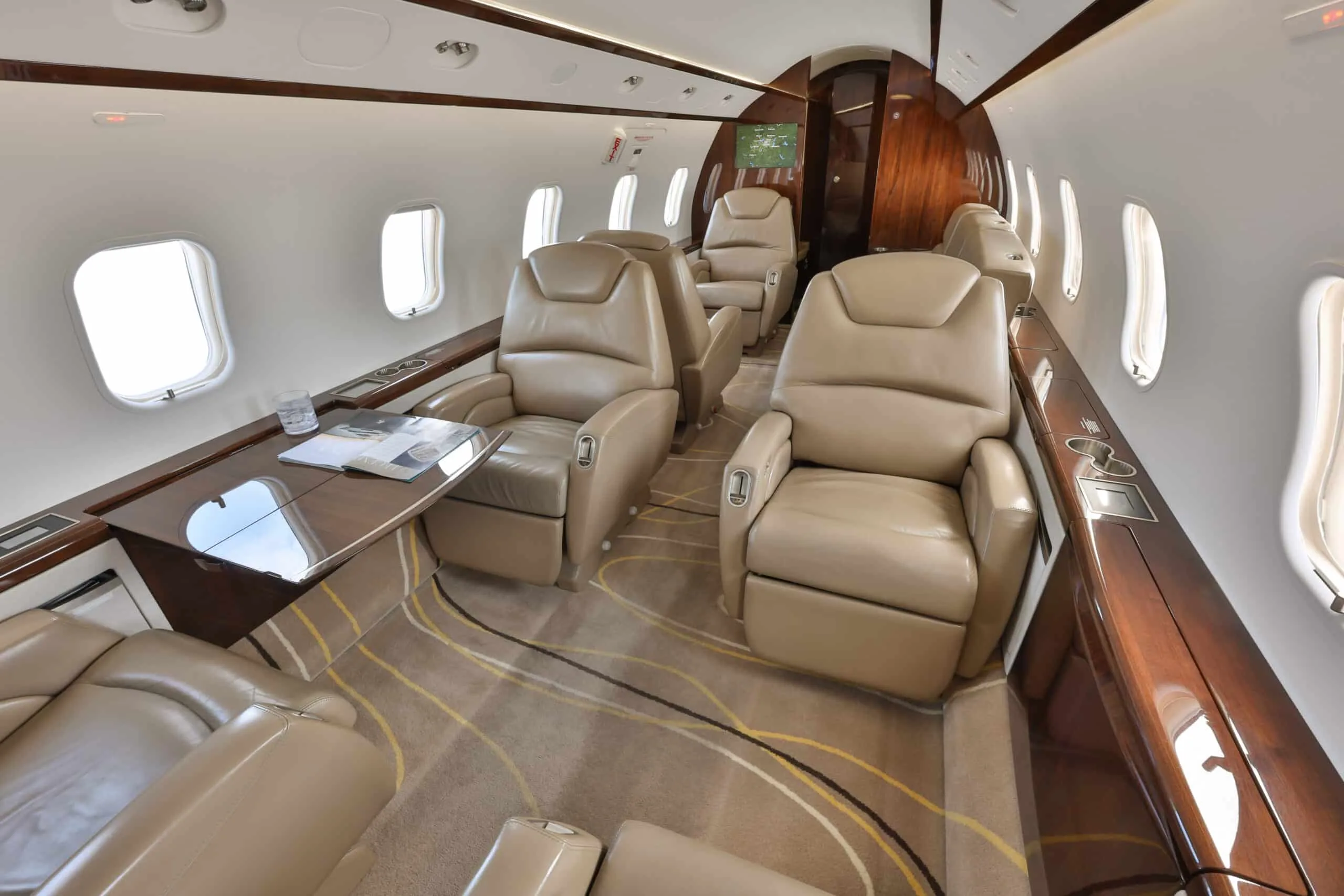 An angled view of the private jet cabin highlights beige leather seating arrangements and a table with a magazine.