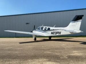 A Beechcraft Bonanza sits on the tarmac in front of a hangar.