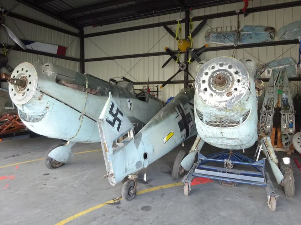 A disassembled Messerschmitt Bf 109 aircraft in a hangar, showing the front and side views.