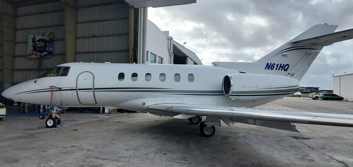 A white business jet with registration N61HQ parked outside a hangar on a cloudy day.