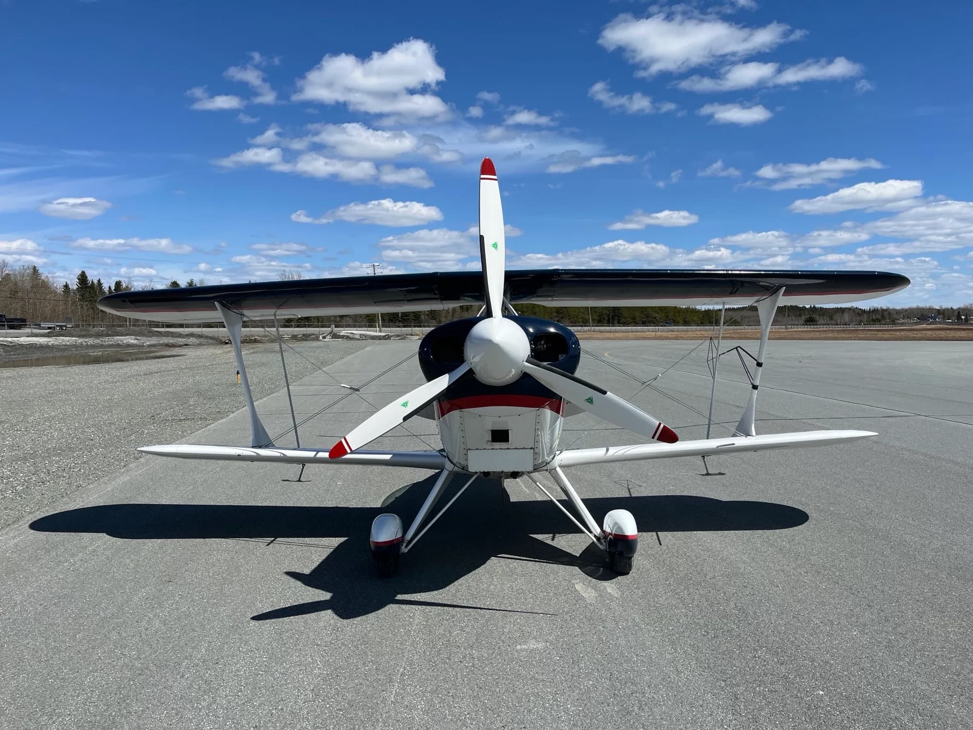 A front view of the dark blue and white Pitts biplane C-GOJF with its propeller facing forward on an asphalt runway.