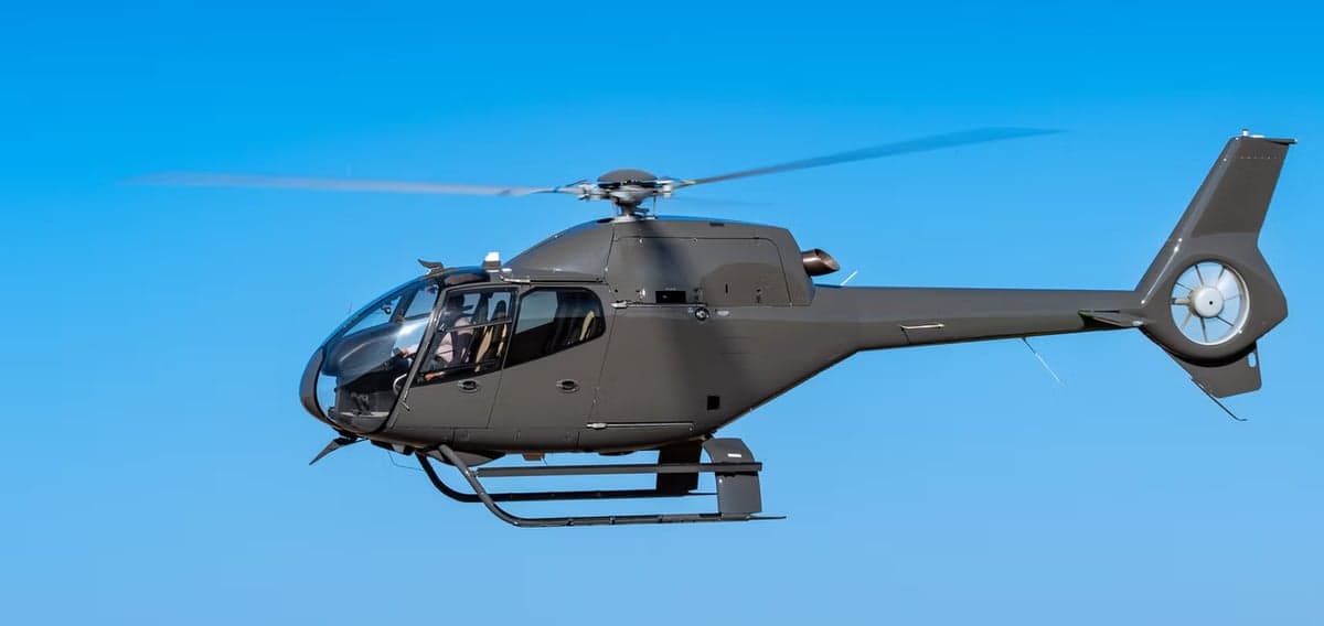 A gray helicopter in flight against a clear blue sky.