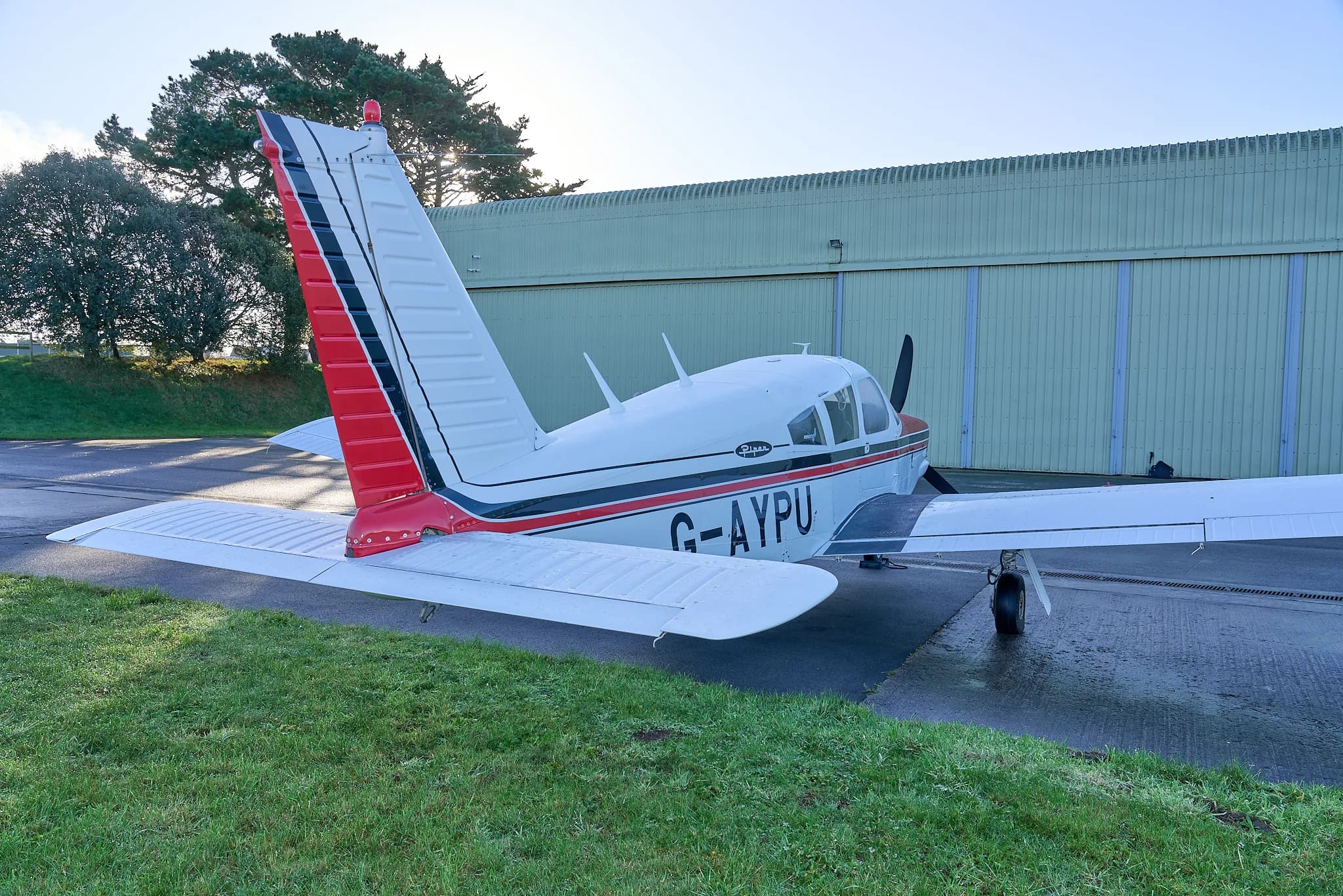 A rear-side view of the white and red Piper Cherokee G-AYPU with its tail facing the camera.