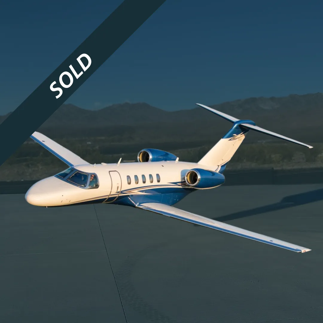 A white and blue Cessna Citation jet is shown on a tarmac with mountains in the background.
