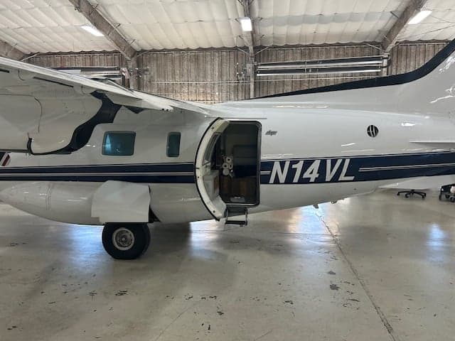 Close up of the side of a white aircraft with black stripes and an open door.