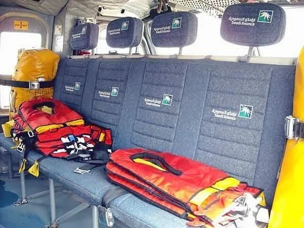 The interior cabin of a helicopter showing passenger seats with Saudi Aramco logos and life vests.