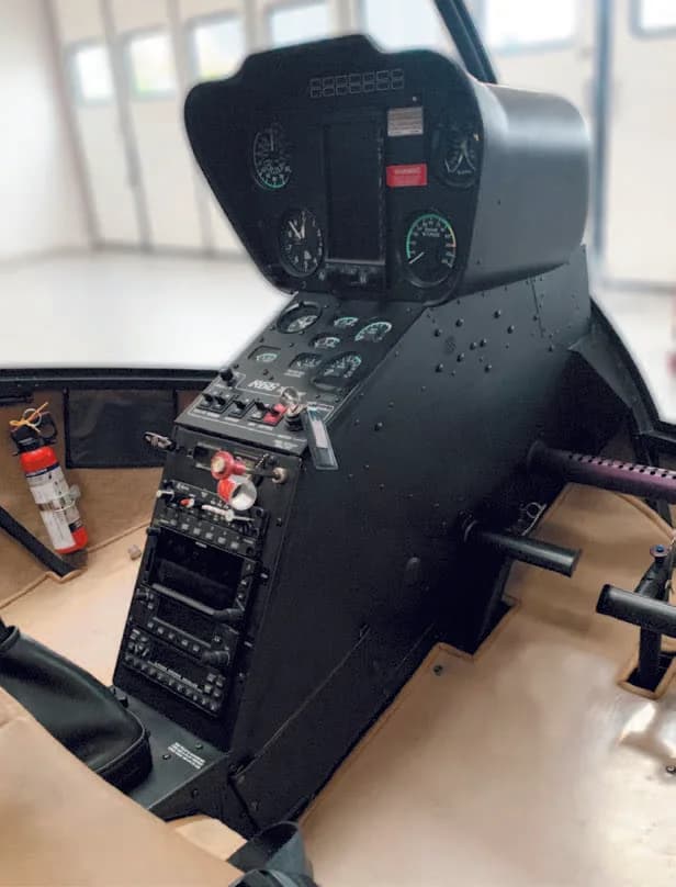 The black instrument panel and central console of a helicopter cockpit, with a fire extinguisher visible.