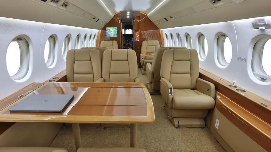 The interior cabin of a business jet featuring tan leather seats and a wooden table with a laptop.