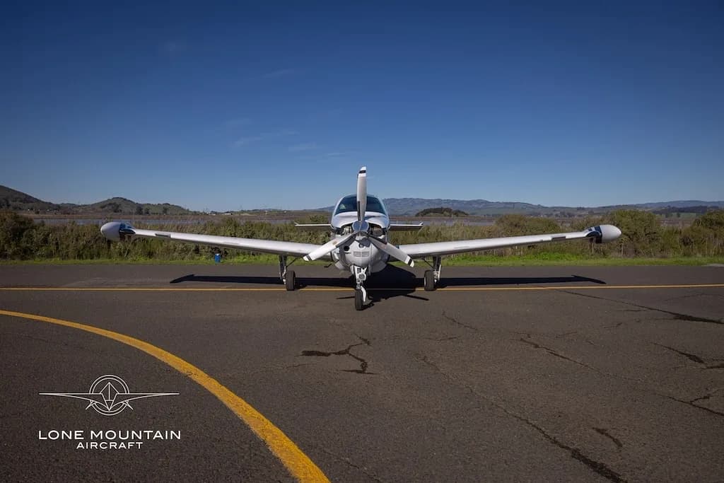 A head-on view of a white Beechcraft Baron N527RS with black and gold stripes parked on an asphalt runway.