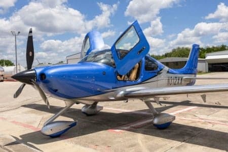 A blue and silver Cirrus SR22 aircraft with its doors open, registration N312XX, parked on an airfield ramp.