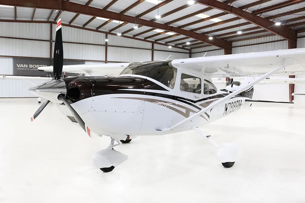 A white and brown Cessna Skylane N788RM is parked in a hangar, viewed from the front-left.