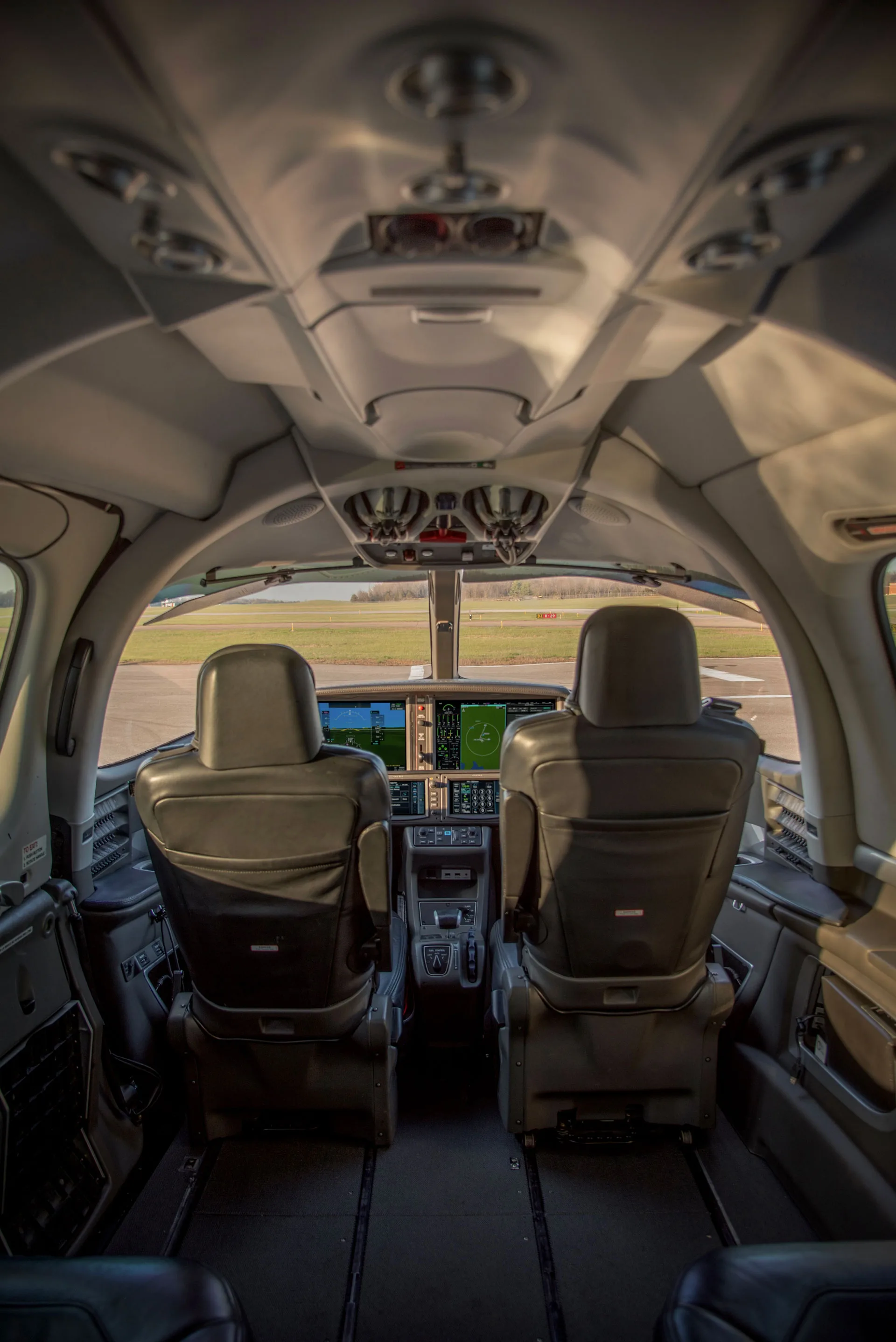 A view from the cabin looking into the cockpit of a Cirrus Vision Jet, showing the two pilot seats and instrument panel.