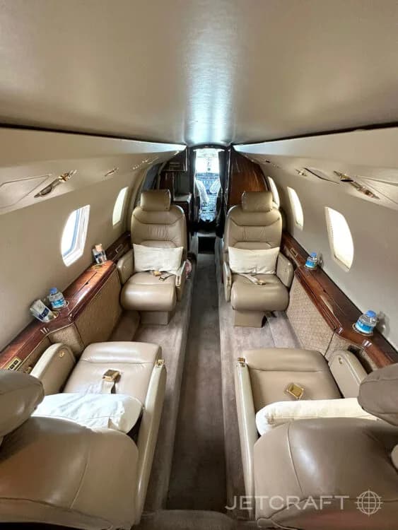 The interior cabin of a business jet, showing tan leather seats and a view towards the cockpit.
