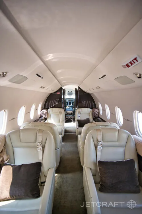 A view of the aircraft cabin aisle with two rows of light-colored leather seats and an "EXIT" sign visible.