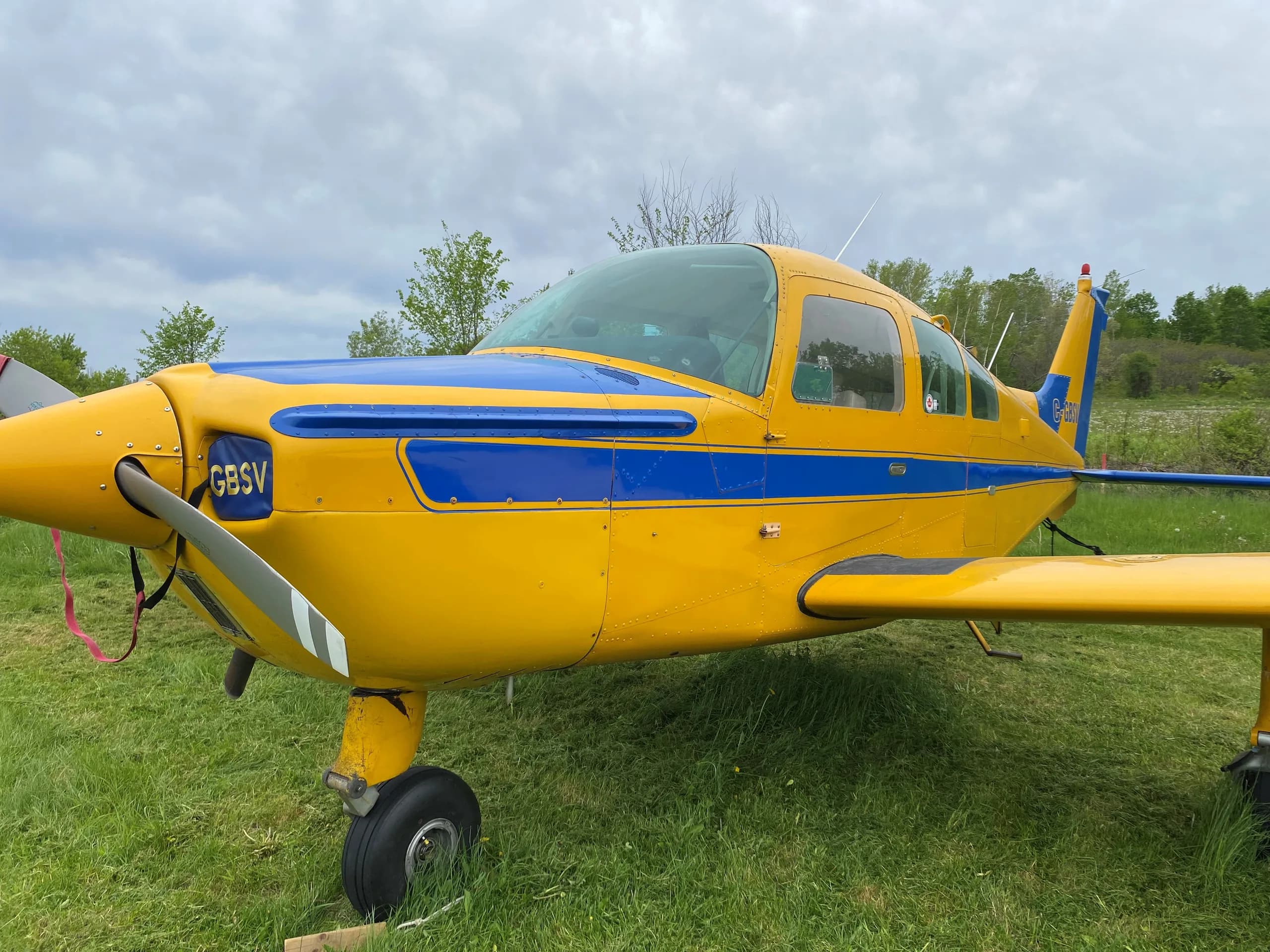A close-up side view of the front of a yellow and blue single-engine aircraft with registration C-GBSV.