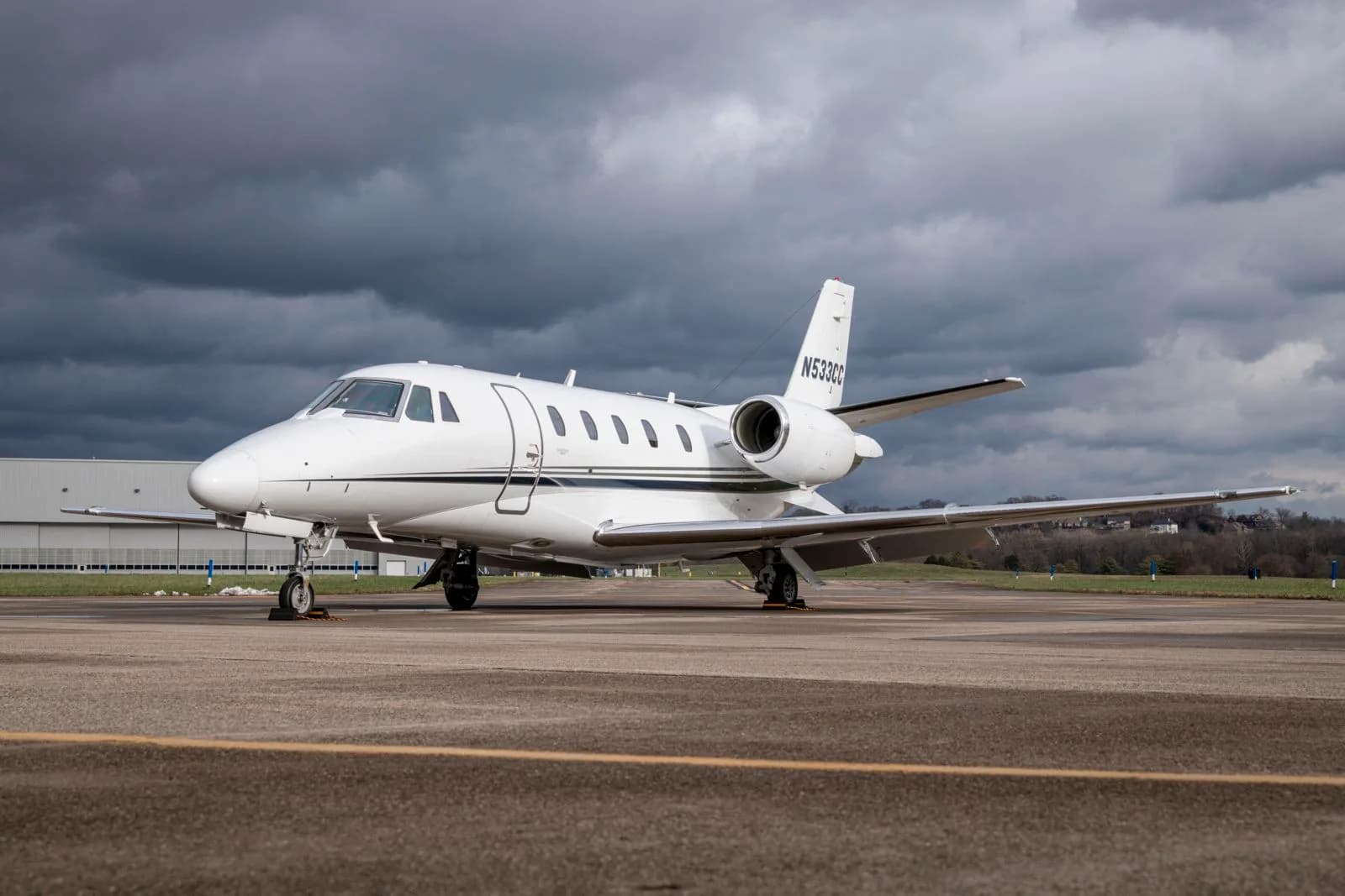 A white business jet with tail number N533CC is parked on an asphalt tarmac under a cloudy sky.