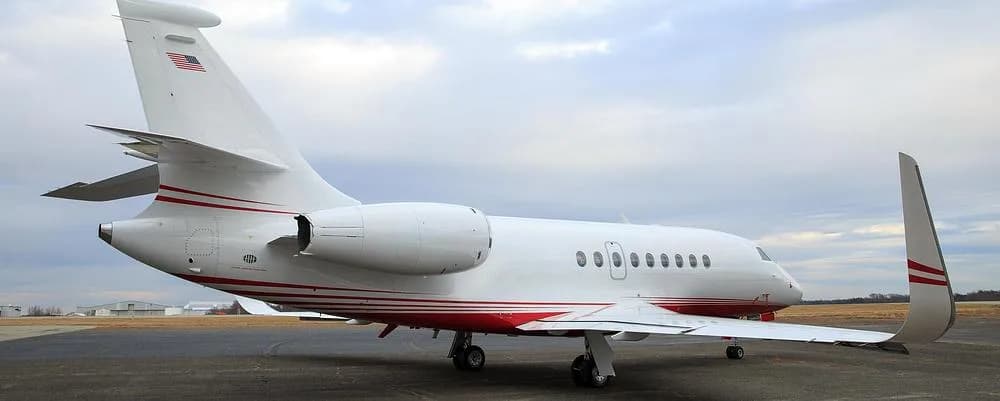 A rear-side view of a white and red Dassault Falcon 900 private jet parked on an airport tarmac.