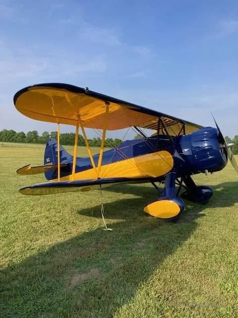 A blue and yellow biplane with registration NC 30124 sits on a green grassy field under a blue sky.