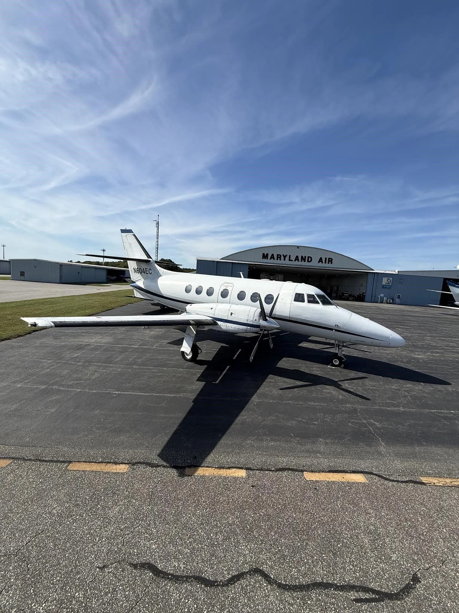 A white Jetstream 31 aircraft with blue accents, tail number N604EC, parked on an asphalt tarmac in front of a "MARYLAND AIR" hangar.