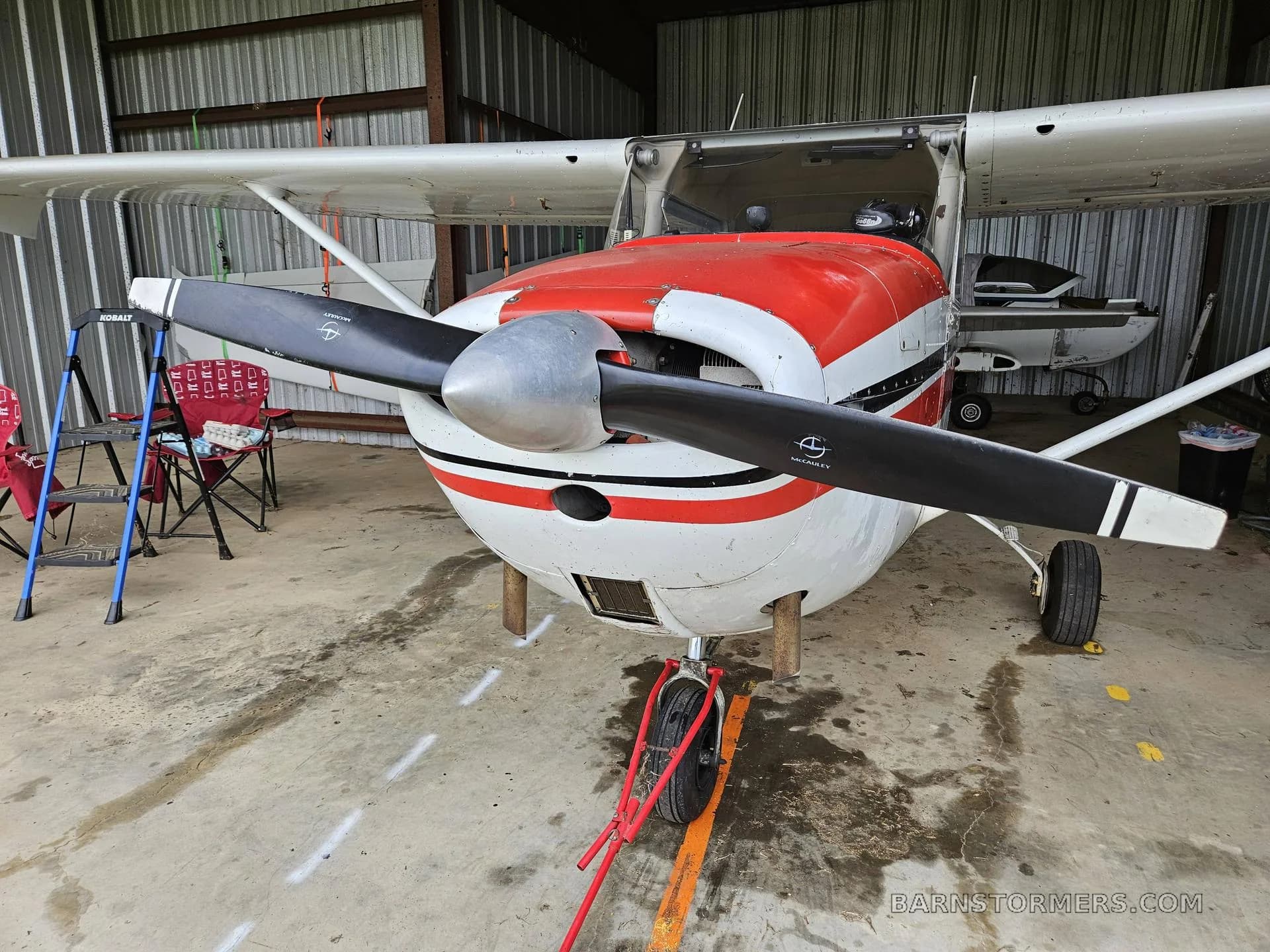 A front view of a white and red single-engine propeller aircraft, N2530Y, parked inside a metal hangar.