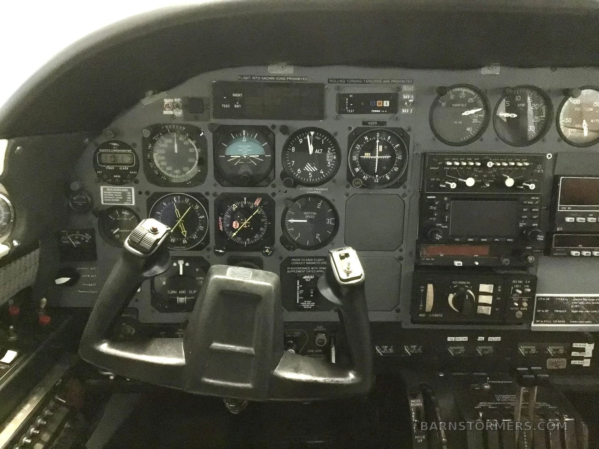 The cockpit instrument panel of an aircraft, featuring analog gauges, avionics, and two control yokes.