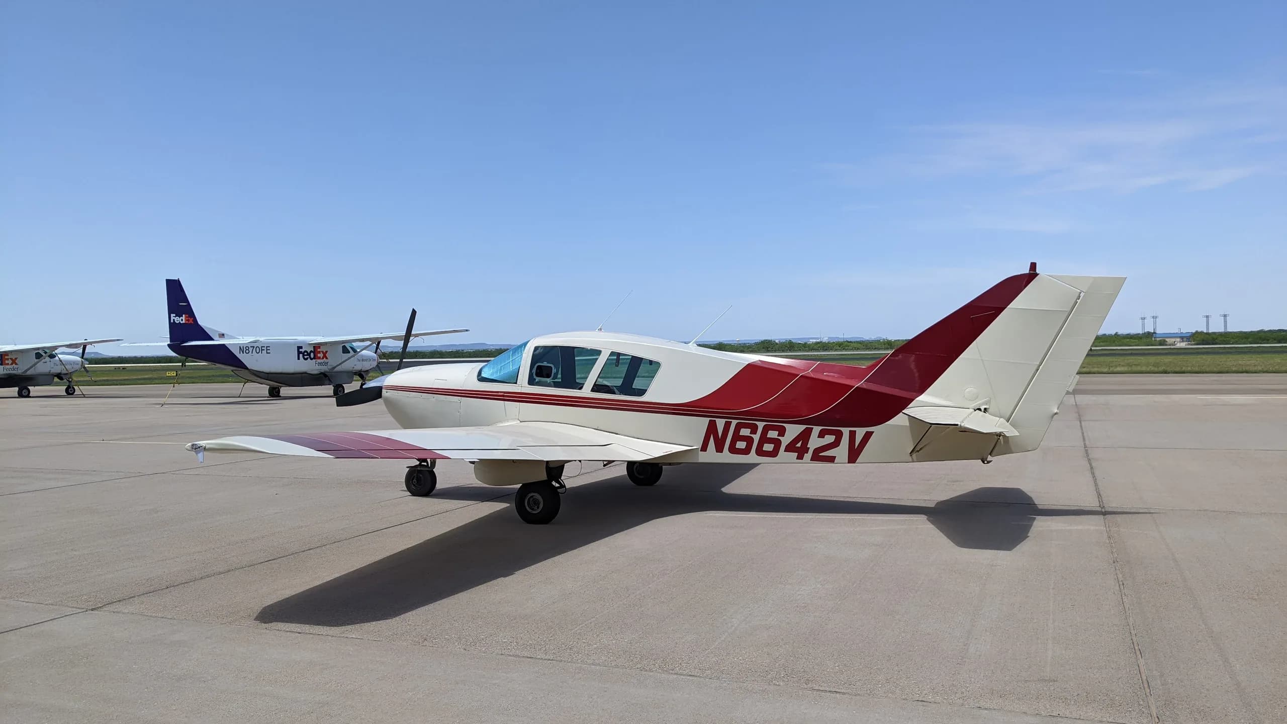 A white and red Bellanca aircraft with tail number N6642V parked on an airfield with other aircraft in the background.