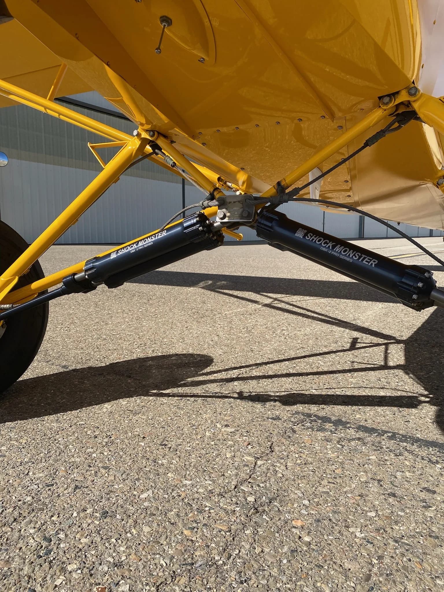 Close-up of the landing gear and suspension of a yellow Carbon Cub aircraft.