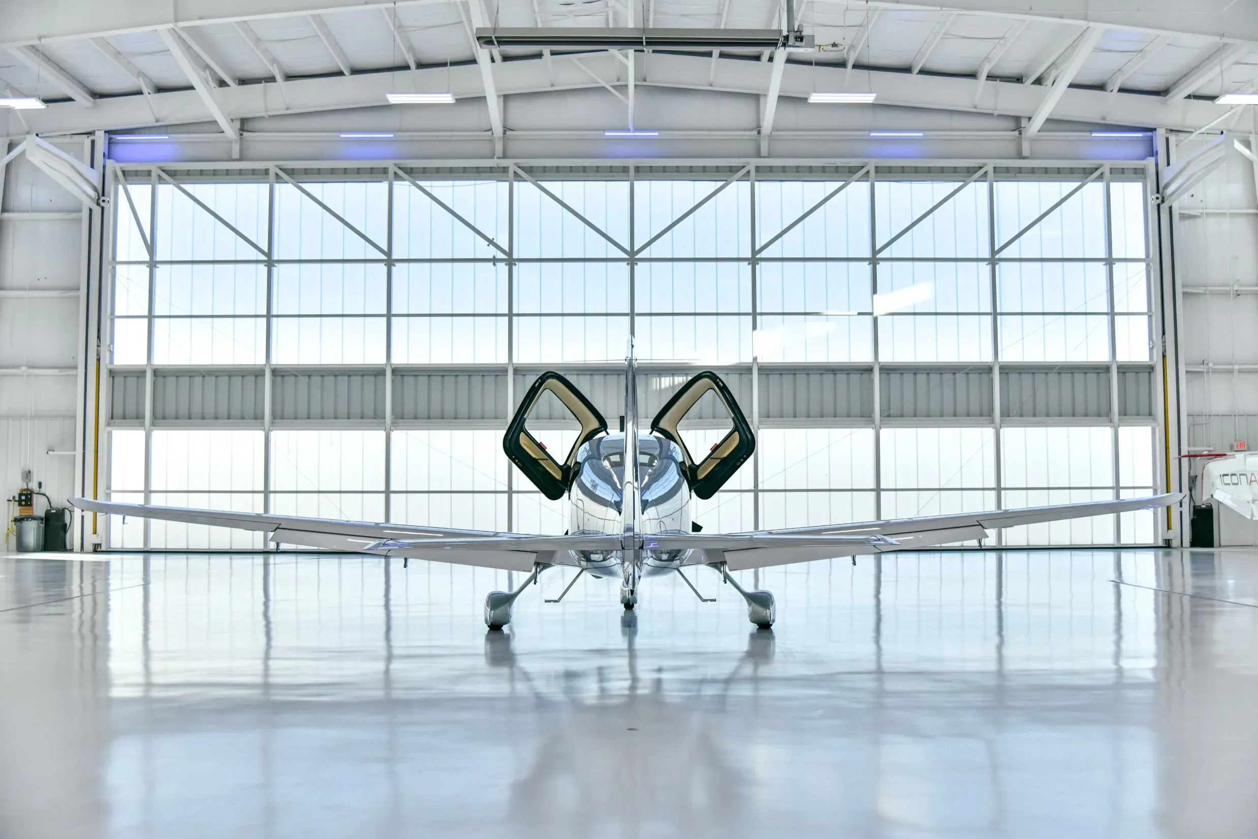 A blue and white Cirrus SR22 aircraft with registration N322LT viewed head-on in a hangar with its gull-wing doors open.