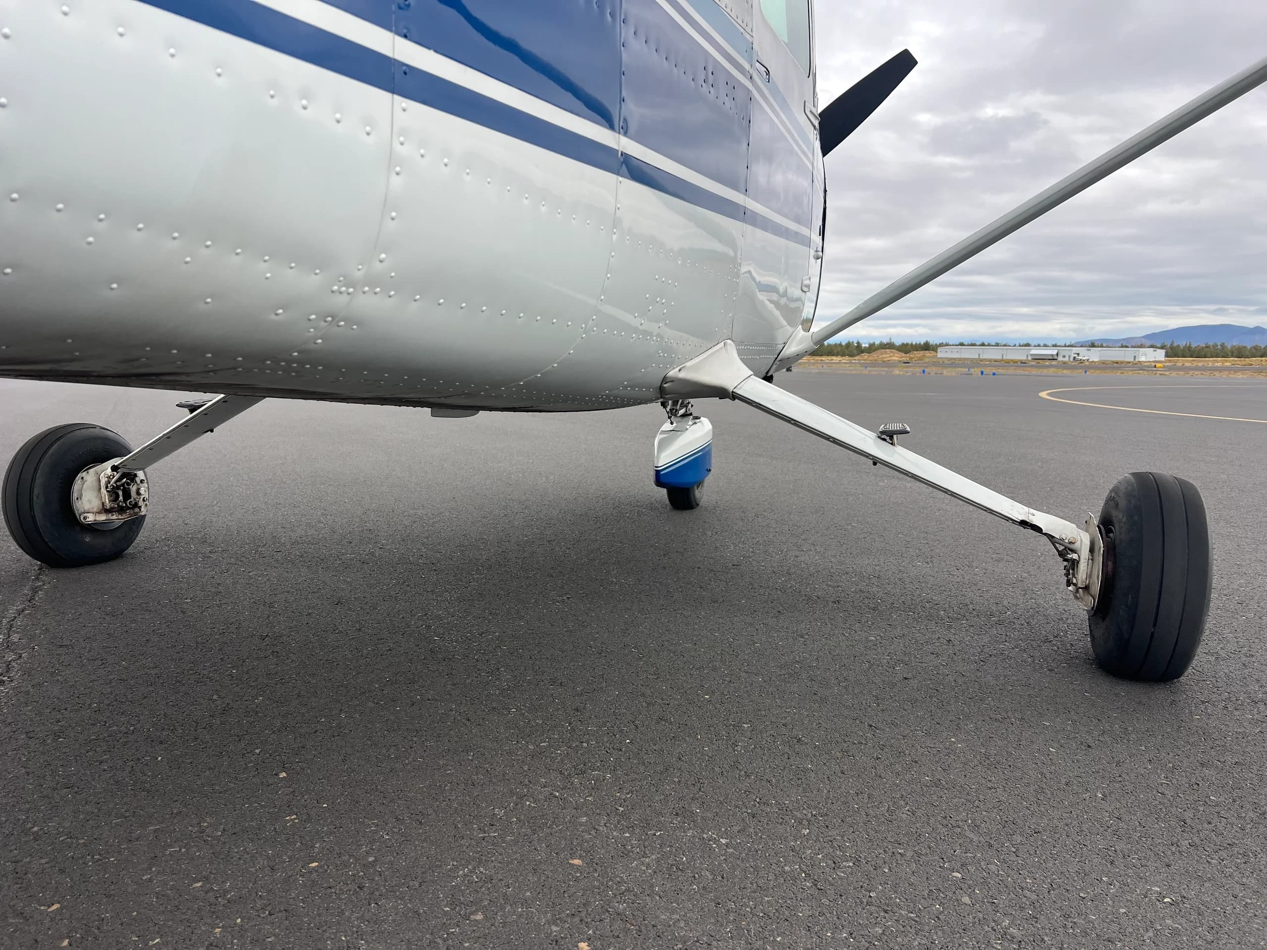 A low-angle view of the main landing gear and lower fuselage of the blue and white Cessna 172 aircraft.