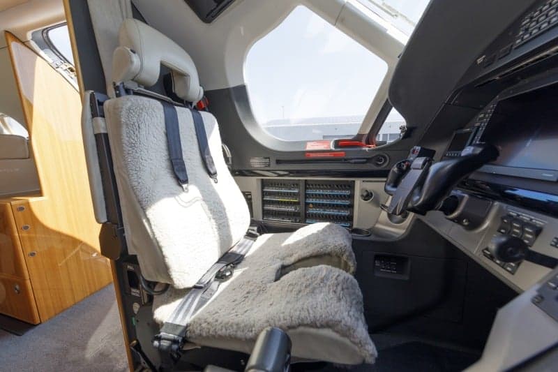 The interior of a Pilatus PC-12 aircraft with white leather seats, looking towards the cockpit.