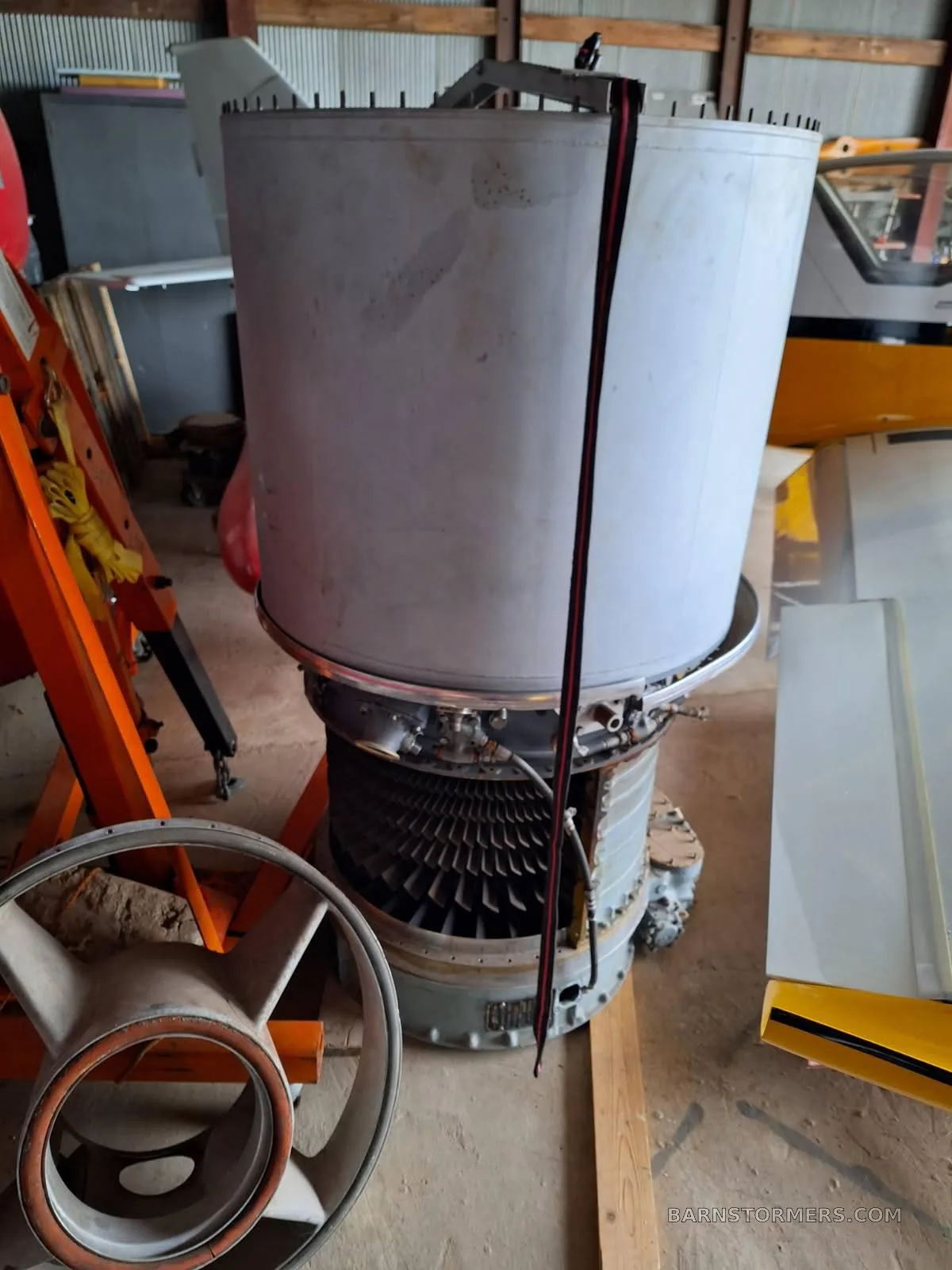 A large, disassembled jet engine with visible turbine blades sits on the floor of a hangar.